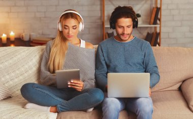 Aletler. Kulaklıklı çift içeride koltukta oturan dizüstü bilgisayar ve dijital tablet kullanıyor. Seçici Odaklanma