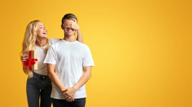 Genç kız erkek arkadaşı için sürpriz yapma ve sarı arka plan üzerinde gözlerini kapama, uzay kopyalamak