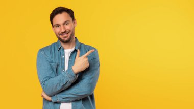 Kısa kahverengi saçlı ve sakallı bir adam fotokopi alanını gösterirken kameraya gülümsüyor. Mavi bir kot gömleğin altına beyaz bir tişört giyiyor ve kollarını kavuşturuyor. Arkaplan sarı.