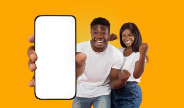 Parlak sarı bir arka planın önünde mutlu bir siyah çift duruyor. Adam elinde beyaz ekranlı akıllı bir telefon tutuyor. Parmağını geniş bir gülümsemeyle ona doğrultuyor.