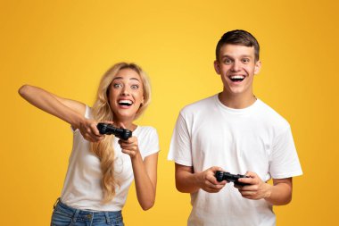 Kumarbaz genç çift joysticklerle video oyunu oynuyor, sarı stüdyo arka planı fotokopi alanı ile.