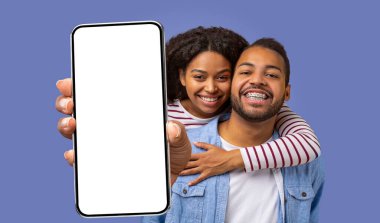 Gülümseyen siyah bir çift mavi bir arkaplanda poz veriyor. Kadın adamın arkasında duruyor ve kollarını adamın omzuna atıyor. Önlerinde boş bir akıllı telefon ekranı tutuyor.