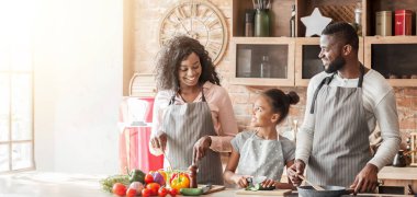 Tatlı küçük Afrikalı kız sebze kesiyor, ailesine akşam yemeği için yardım ediyor, evde birlikte yemek pişiriyor, yer kopyalıyor.