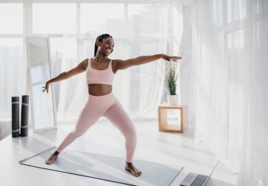 Spor giyim bölümünde formda bir Afrikalı Amerikalı kadın yoga yapıyor, ev içi spor yapıyor, spor salonunda video çekiyor, fotokopi çekiyor. Güzel siyahi kadın ev işlerinden hoşlanıyor.