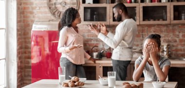 Aile sorunları konsepti. Afrika kökenli Amerikalı küçük bir kız elleriyle gözlerini kapatıyor. Ebeveynler kahvaltıda, fotokopi çekerken...