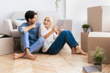 Ev Taşınma. Yeni apartmandaki taşınan kutuların arasında duran Tablet Bilgisayarı kullanarak Rahatlamış Çift.