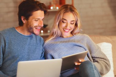 Modern İlişki. Rahat çift tablet ve dizüstü bilgisayarları kullanarak kanepede kapalı oturan. Seçici Odak