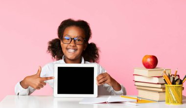 Neşeli Siyah İlköğretim Öğrenci Kız Studio, Sarı Arka Plan Masada Oturan Boş Ekranda Tablet İşaret Parmak Gösteren. Mockup