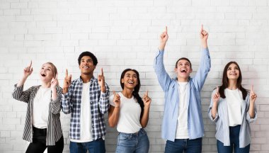 Eğitim konsepti. Beyaz tuğla duvarın üzerinde boş alanı işaret eden gençler