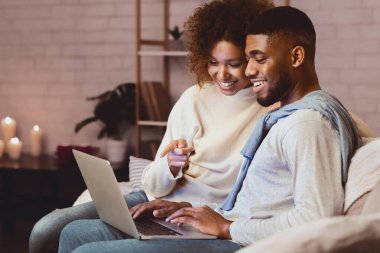 Sevgili Afro çift dizüstü bilgisayarda film seçiyor, sıcak kış akşamında birlikte dinleniyorlar, boş yer var.