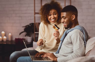 Çevrimiçi bankacılık. Kadın, erkeğe internet alışverişi yaptırıyor, elinde kredi kartı tutuyor ve dizüstü bilgisayarını işaret ediyor.