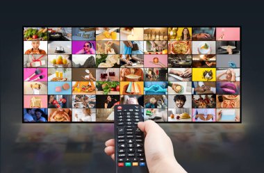 Bir kişi uzaktan kumandayı tutuyor ve onu büyük bir düz ekran televizyona doğrultuyor. TV ekranı bir ızgara biçiminde çeşitli renkli, çeşitli içerikleri gösterir
