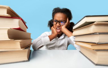 Misbehavior At School. Naughty Black Schoolgirl Sitting At Books Bored Of Doing Homework Over Yellow Studio Background clipart