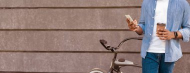 Bilinçsiz siyah adam bisikletin yanında duruyor kahve ve akıllı telefonla rahatlıyor, kırpılmış görüntü