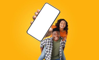 Afro-Amerikalı genç çift gülümsüyor ve kameraya bakıyor. Kadın önünde boş bir ekranla büyük bir akıllı telefon tutuyor.