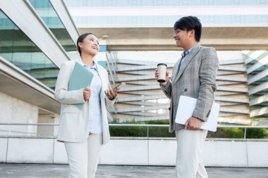 Resmi giyinmiş iki Asyalı iş adamı, çağdaş bir ofis binasının önünde dostça sohbet ediyorlar..