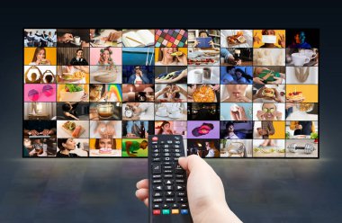 Bir el geniş bir ekranın önünde siyah bir TV kumandası tutuyor ve çeşitli görüntüler gösteriyor. Ekranda yemek yiyen, çalışan ve rahatlatan insanlar da dahil olmak üzere çeşitli sahneler gösteriliyor..