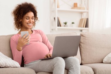 Teknoloji aletleri, dizüstü bilgisayar ve cep telefonu kullanan mutlu bir kadın. Kanepede dinleniyor.