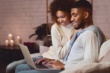 Heyecanlı afro çift dizüstü bilgisayarda sörf yapıyor. Evdeki sıcak kış atmosferinin tadını çıkarıyor.