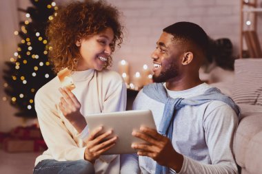 Noel için hazırlanıyorum. Heyecanlı Afrikalı çift, tablet ve kredi kartı kullanarak internetten hediye alıyor.