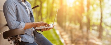 Tanımlanamayan siyah adam bisiklete yaslanıyor ve dizüstü bilgisayar kullanıyor, yan görüş, boş alan ile kırpılmış görüntü.