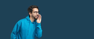 Mavi kapüşonlu genç bir adam tutkulu bir şekilde boşluğu kopyalamak için bağırıyor, coşkusunu dile getiriyor. Gözlükleri yüzünü çerçeveliyor, hafifçe öne eğiliyor, canlandırıcı bir his veriyor.