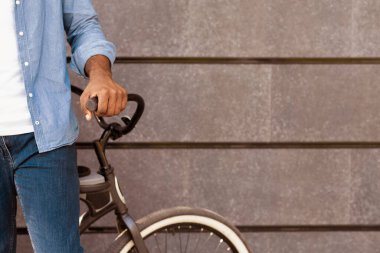 Tanımlanamayan Afrikalı Amerikalı bisikletinin yanında duran gri duvar arka planı, kopyalama alanı