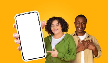 Siyah kadın ve erkek kameraya gülümserken elinde boş bir ekranla akıllı telefon tutuyorlar. Kadın yeşil kapüşonlu ve beyaz tişört giyerken, adam bej düğmeli gömlek giyiyor.