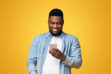 Gülümseyen Afrikalı Amerikalı adam akıllı telefondan fotokopi çekilen sarı arka plan üzerinden mesaj okuyor.