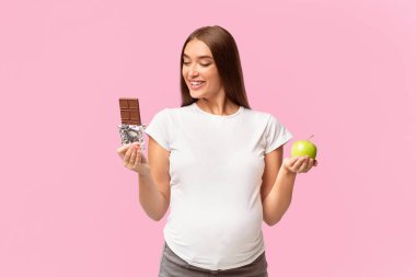 Hamilelik Beslenmesi. Çikolata ve elma taşıyan hamile bir kadın beyaz arka planda durmayı tercih ediyor. Stüdyo Çekimi
