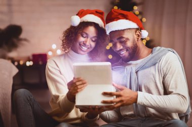 Noel büyüsü. Afro çift rahat oturma odasında hediye kutusu açıyor, geceyi birlikte geçiriyorlar.