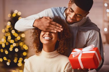 Mutlu afro adam kız arkadaşına Noel hediyesi veriyor, sürpriz yapıyor ve gözlerini kapatıyor.