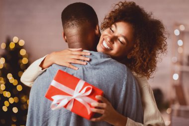 İyi tatiller. Minnettar afro kadın Noel hediyesi ile evde kocasına sarılıyor.