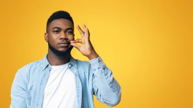 Sessiz bir konsept. Çekici Afrikalı Amerikalı adam ağzını kapayıp sarı arka planda sırrını söylemeyeceğine söz veriyor.