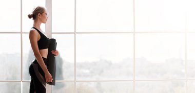 Yoga yapmaya hazır, yoga minderi tutan, beyaz çatı katı stüdyosu arka planı, fotokopi alanı