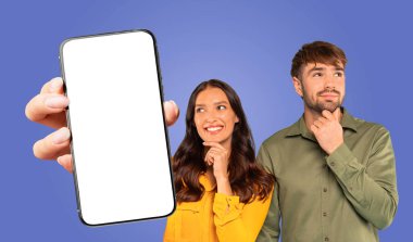 Bir kadın mavi arkaplan önünde boş ekranlı akıllı telefonu tutuyor. Gülümsüyor ve ekrana bakıyor. Yanındaki adam çenesini tutarken yukarı bakıyor.