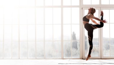Stüdyoda yoga yapan genç ve güzel bir kadın. Büyük pencereli.