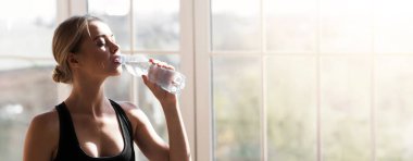 Yoga stüdyosunda büyük pencereli egzersiz yaparken, sportif kızın içme suyunu kapat, boşluğu kopyala