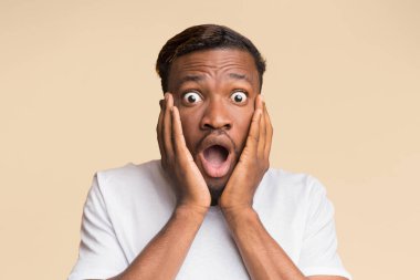 Omg. Surprised Black Man Touching Face Looking At Camera In Shock Posing Over Orange Background. Studio Shot