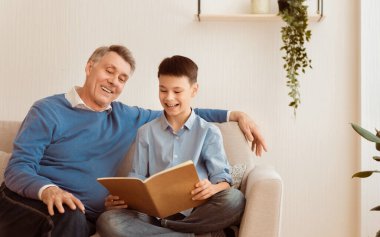 Neşeli büyükbaba, torunuyla kitap okuyor. Ödev yapıyor. Evde, koltukta oturuyor. Seçici Odaklanma, Boş Alan