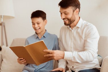 Mutlu çocuk ve sevecen baba evde koltukta oturmuş kitap okuyorlar. Baba-oğul ilişkisi. Seçici Odaklanma