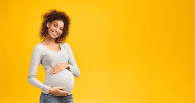 True mother love. African-american pregnant woman hugging her belly and smiling to camera, pink background with free space