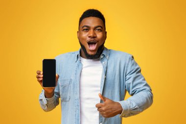 Vay canına, harika bir uygulama. Şaşırmış Afrikalı adam elinde siyah ekranlı akıllı telefon tutuyor ve baş parmağını kaldırıyor, sarı arka planda boş alan var.