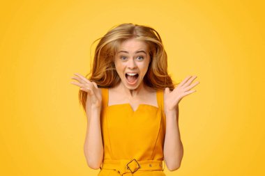 Heyecanlı genç kız, sarı arka planda sevinçle çığlık atıyor kameraya bakıyor ve ellerini kaldırıyor.