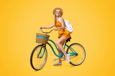 Yaz Modu. Klasik bisiklete binen ve Sarı Stüdyo Arkaplanında Gülümseyen Şık Genç Kızın Uzun Boylu Portresi