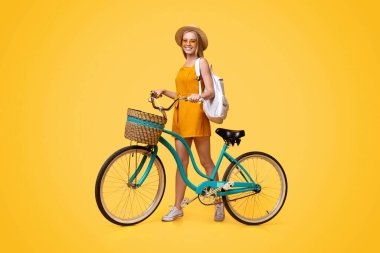 Yaz gezisi. Stüdyoda sarı arka planda klasik bisiklet pozu veren şık hippi kız kameraya bakıyor ve gülümsüyor.