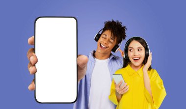 Beyaz gömlekli genç bir siyah adam arkasında duruyor, kulaklıkla müzik dinliyor ve elinde boş ekranlı bir akıllı telefon tutuyor.