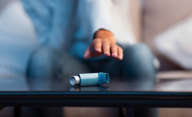 Astım krizi geçiren genç bir kadın astım spreyine ulaşıp evdeki kanepede oturuyor.