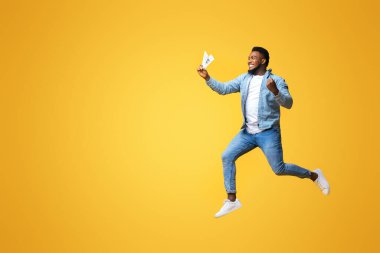 Parayı geri ver. Bin yıllık öforik siyahi adam elinde dolar banknotlarıyla zıplıyor, sarı arka plan, serbest alan