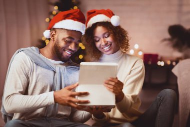 Noel büyüsü. Afro çift rahat oturma odasında hediye kutusu açıyor, geceyi birlikte geçiriyorlar.